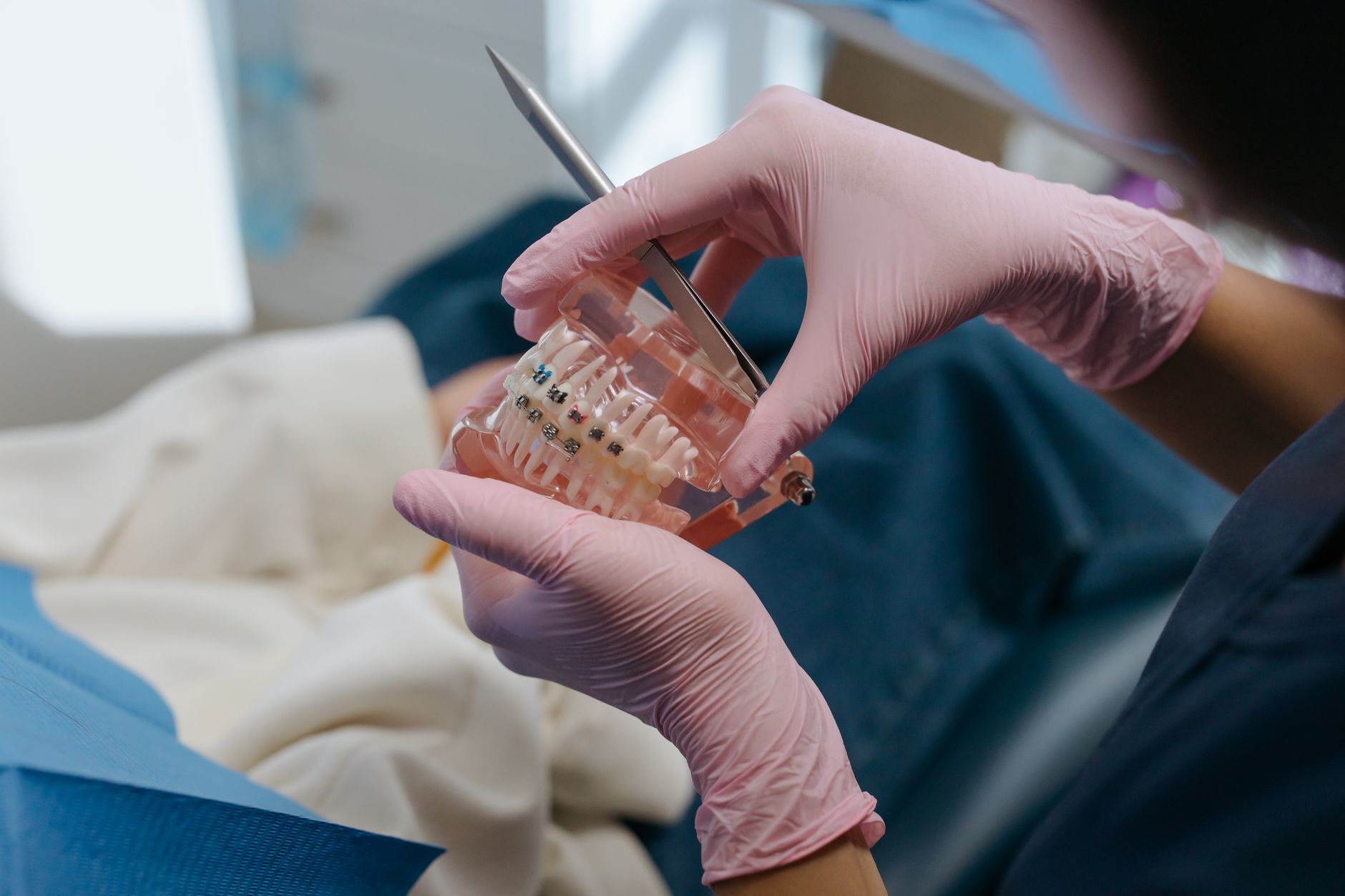 Gloved hands holding a clear teeth model fitted with metal braces