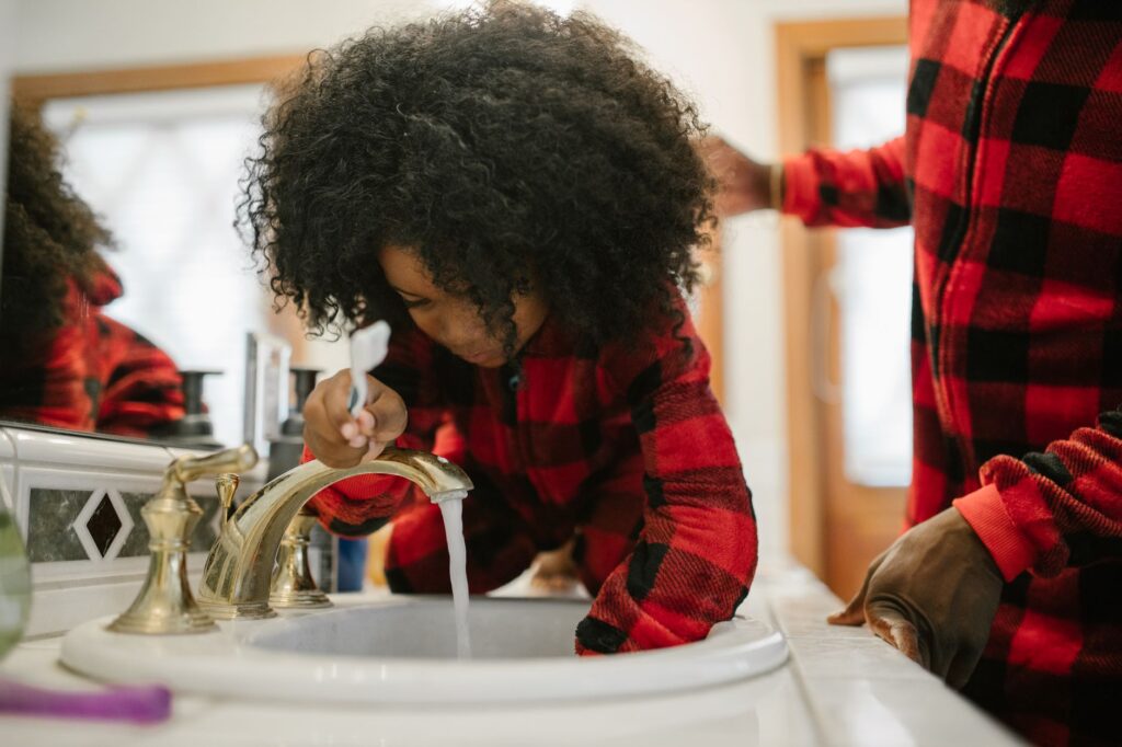 A father helps his daughter brush her teeth at the bathroom sink, highlighting family routines.