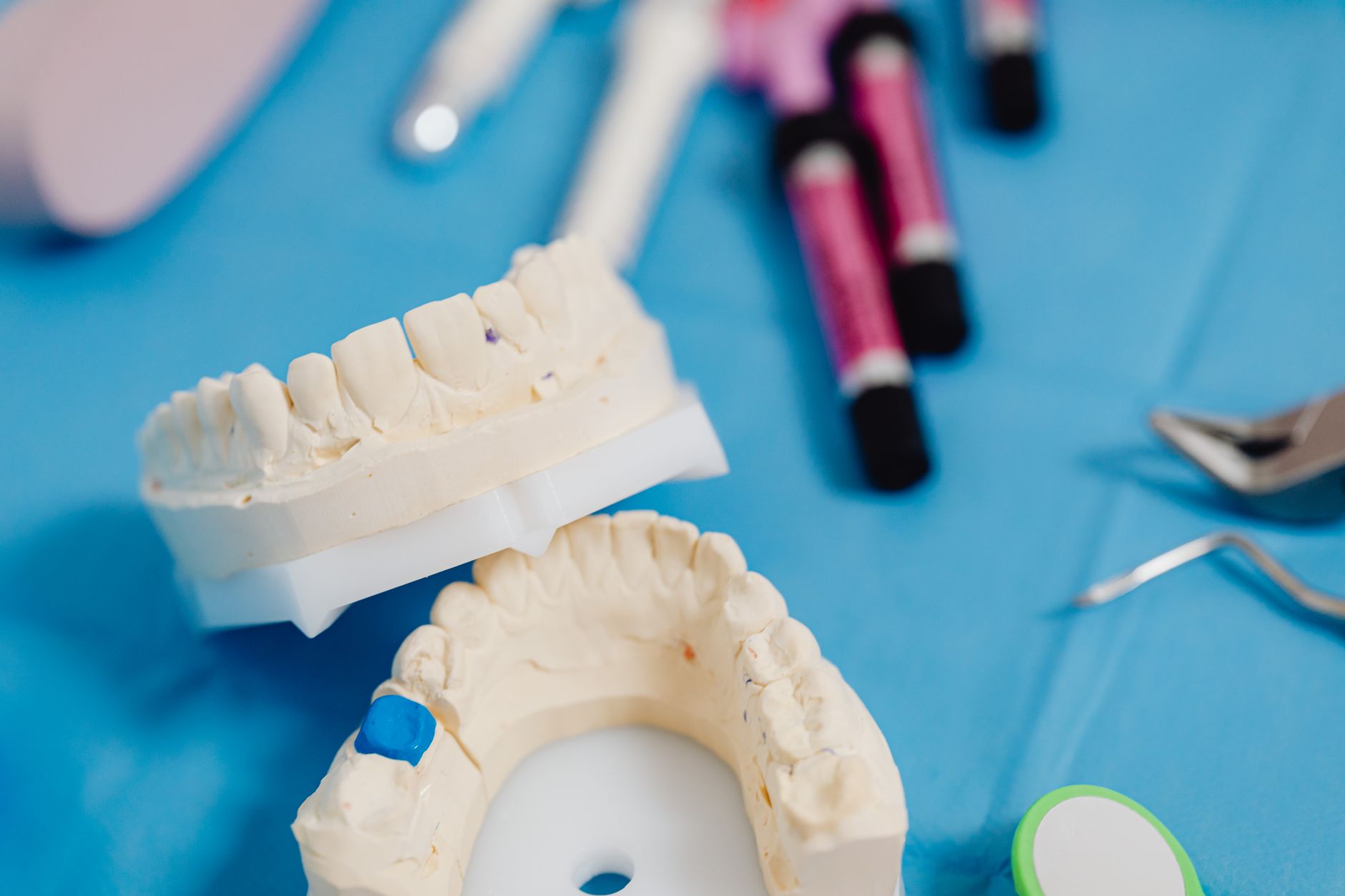 Plaster dental study models of upper and lower teeth on a blue cloth beside dental instruments